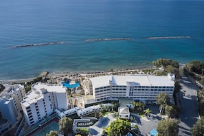 Vista aérea de un hotel frente al mar, con piscina y un cartel que dice 'WELCOME'.