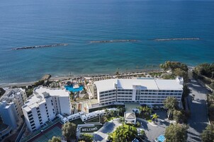 Vista aérea de un hotel frente al mar, con piscina y un cartel que dice 'WELCOME'.