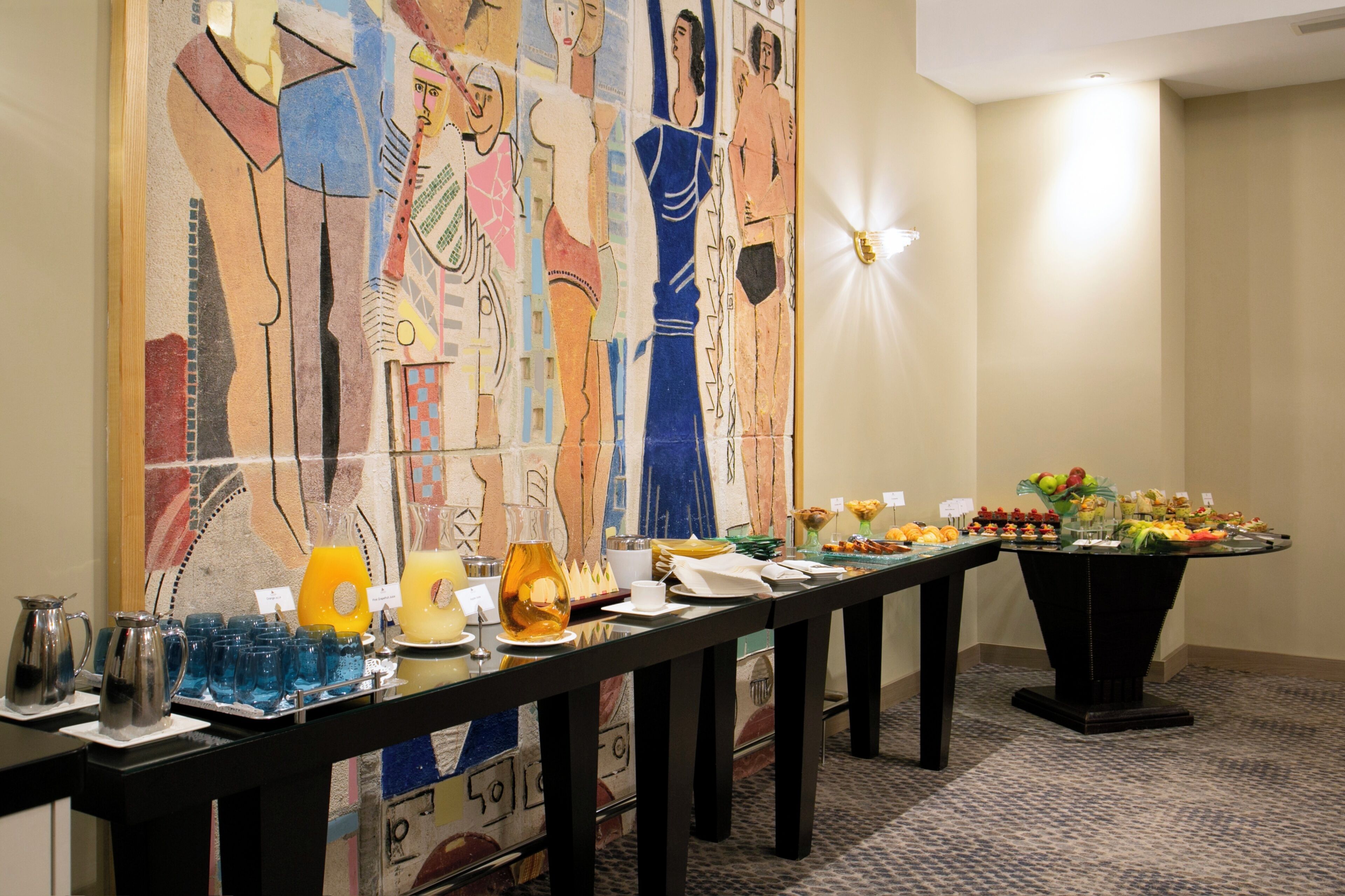 A buffet table with various food items and beverages, a wall with abstract art, and a carpeted floor.