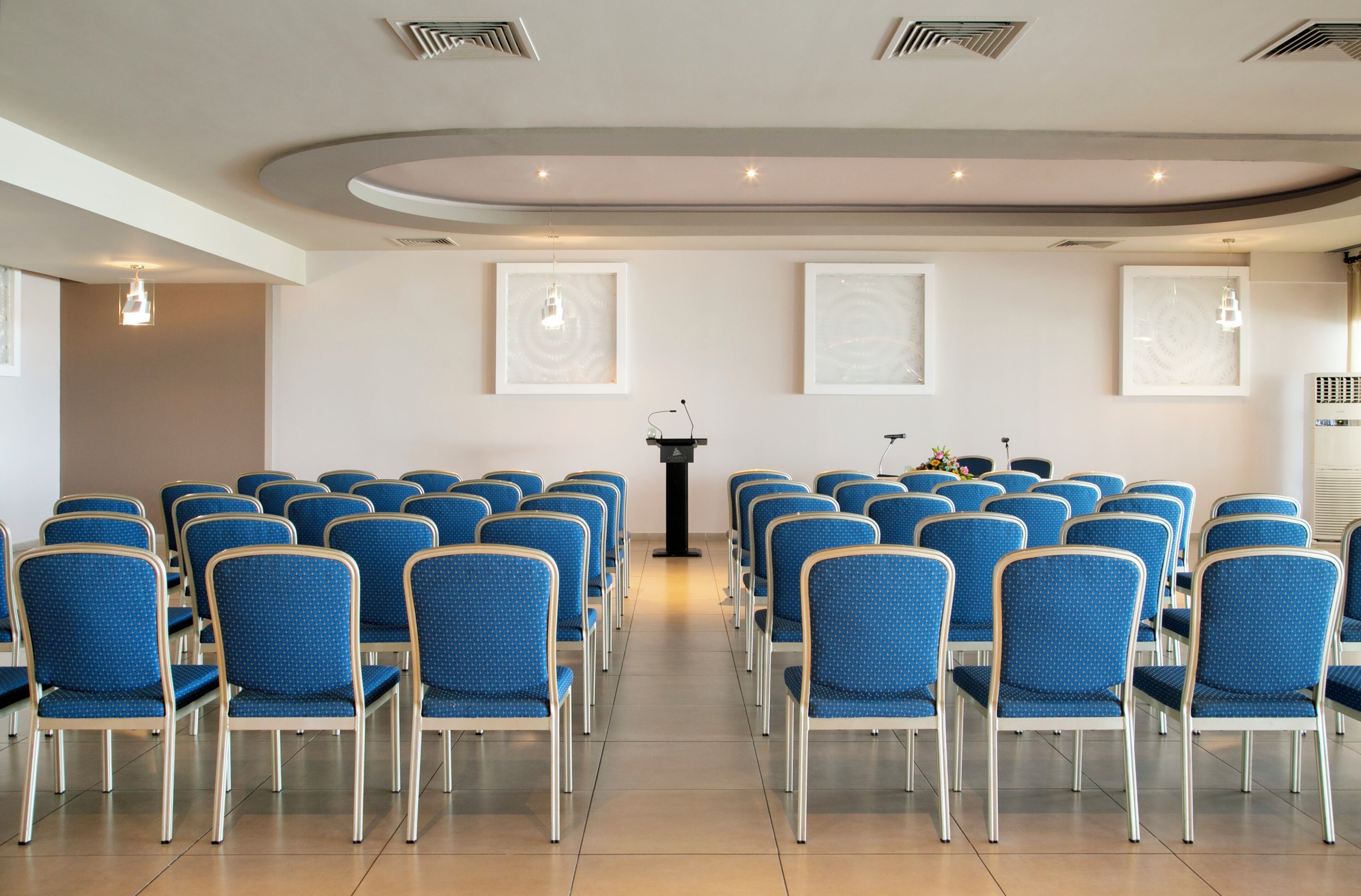 A conference room with rows of chairs, a podium, and ceiling lights.