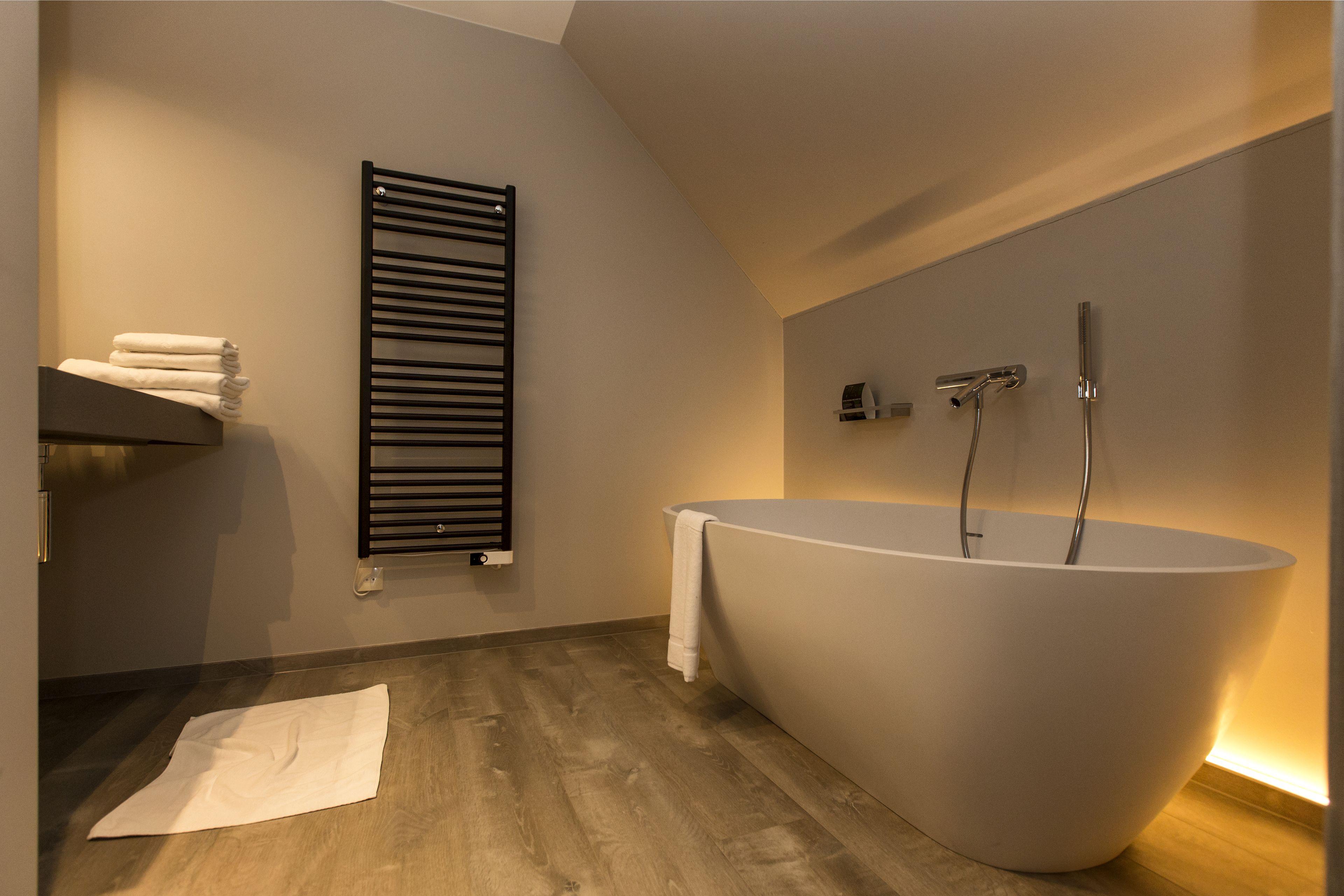 A modern bathroom with a freestanding bathtub, a towel rack, and a wooden floor.