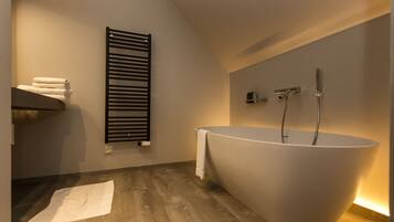 A modern bathroom with a freestanding bathtub, a towel rack, and a wooden floor.