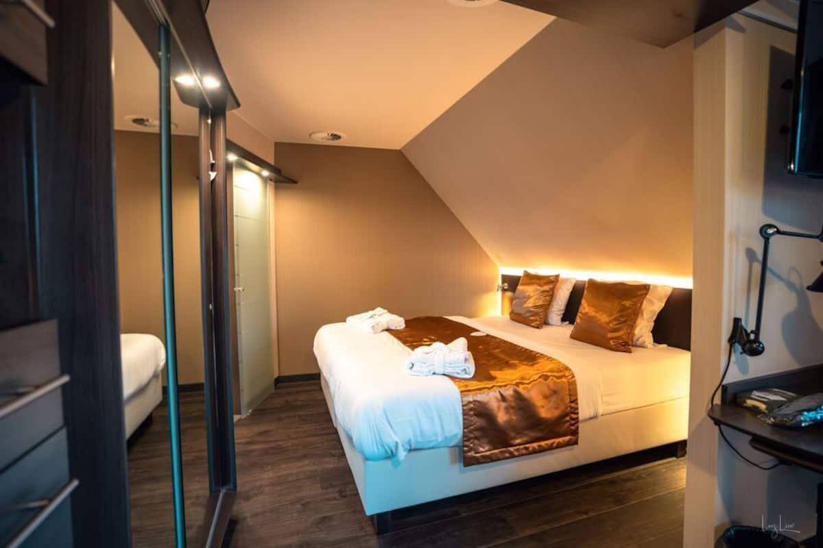 Una habitación de hotel moderna con una cama grande, una mesita de noche, un escritorio y un espejo.