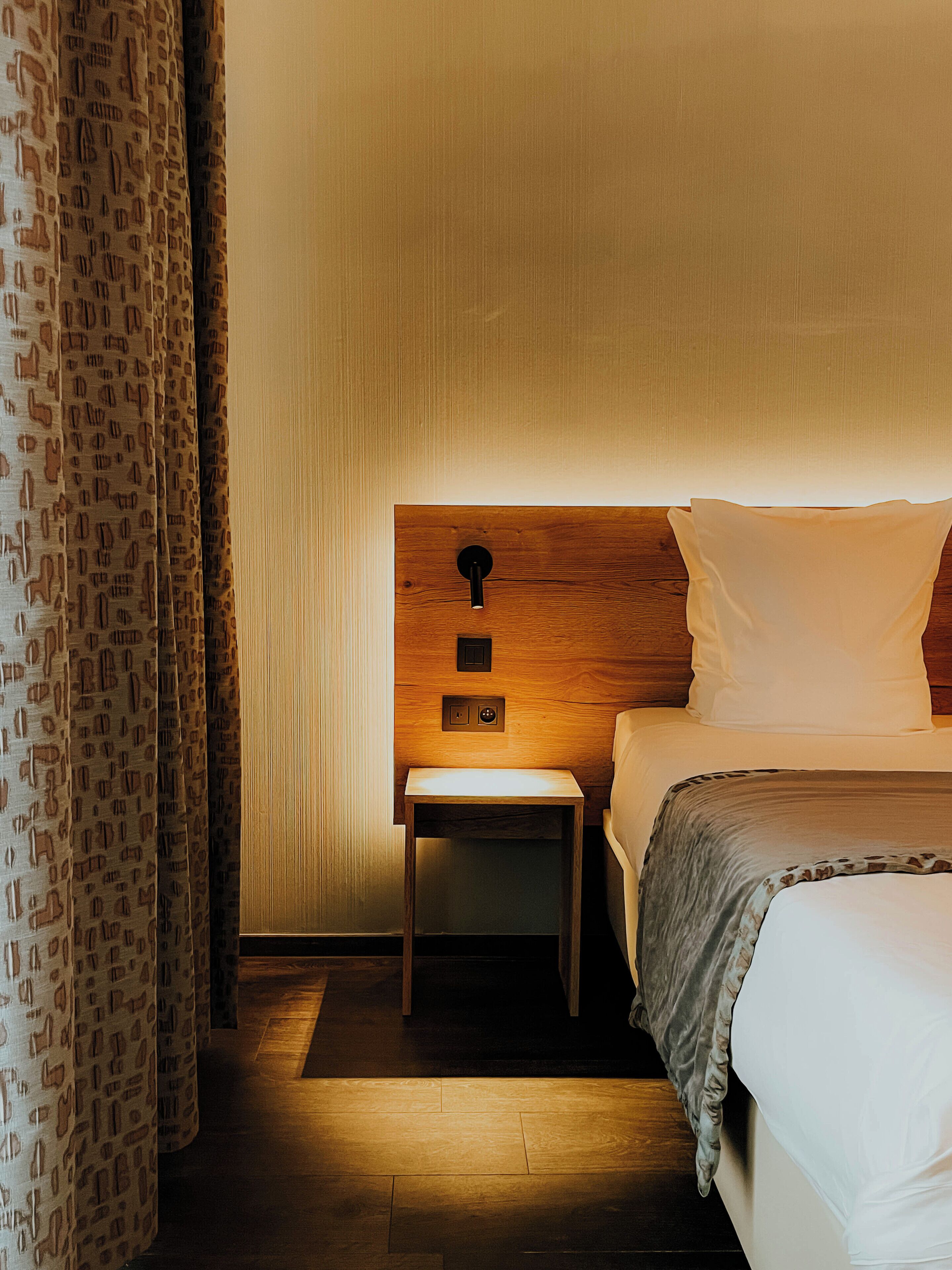 A hotel room with a wooden headboard, a bedside table, and a bed with white bedding.