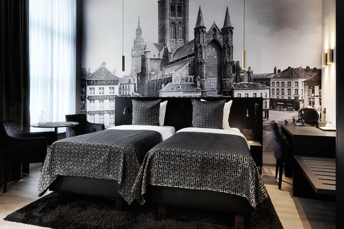 A hotel room with two beds, a large window, a cityscape mural, and a desk with a chair.
