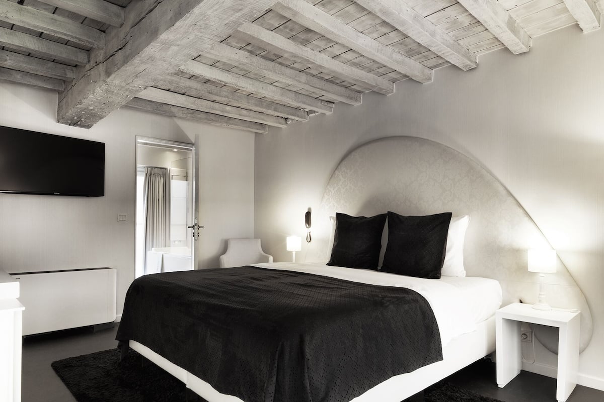 Un dormitorio moderno con una cama grande, mesitas de noche blancas, un televisor de pantalla plana y techo de madera.
