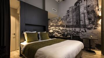 Une chambre d’hôtel moderne avec un grand lit, une petite table et une fresque représentant un bâtiment historique sur le mur.