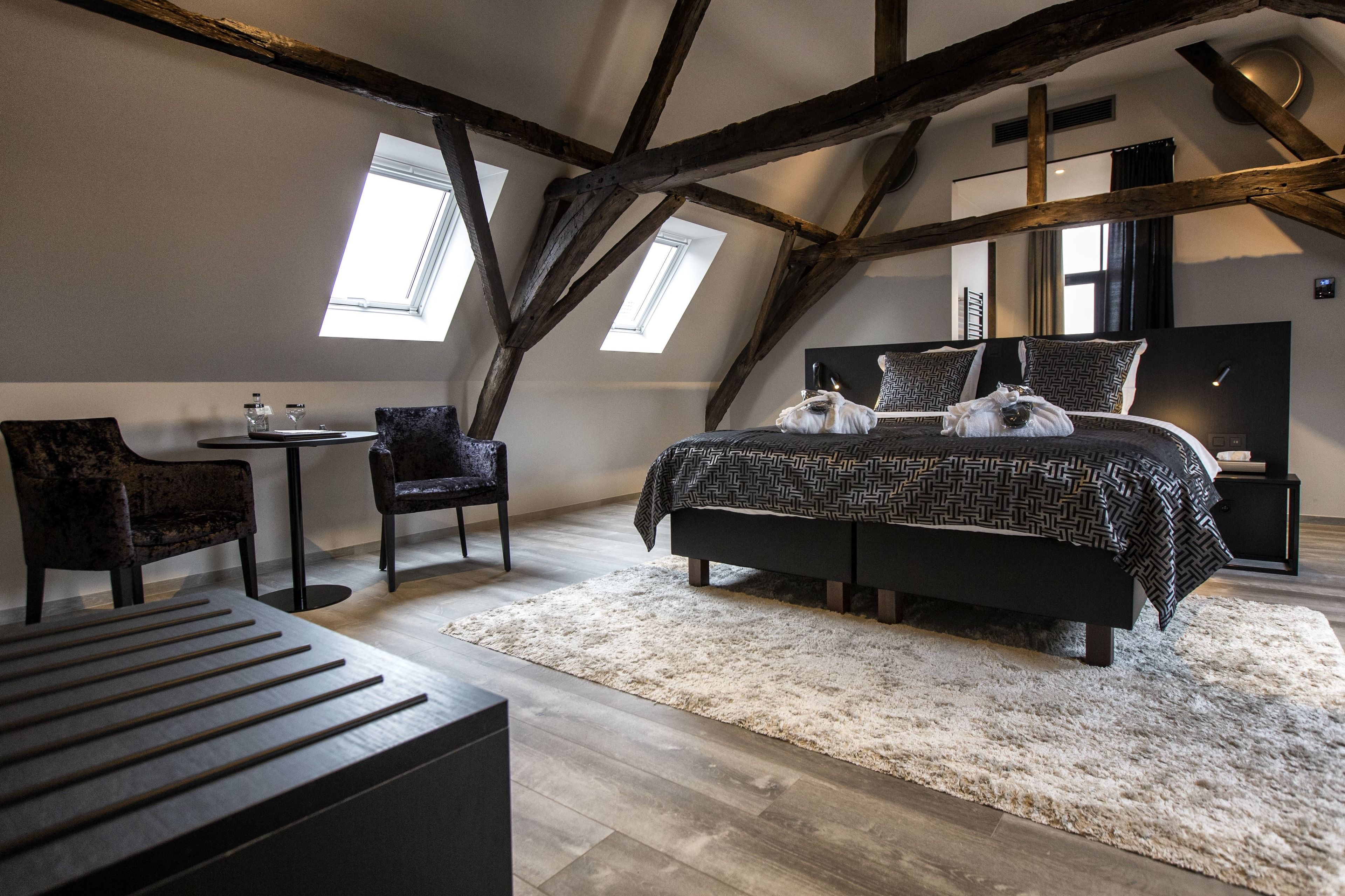 A bedroom with a large bed, two chairs, a small table, and a wooden bench.