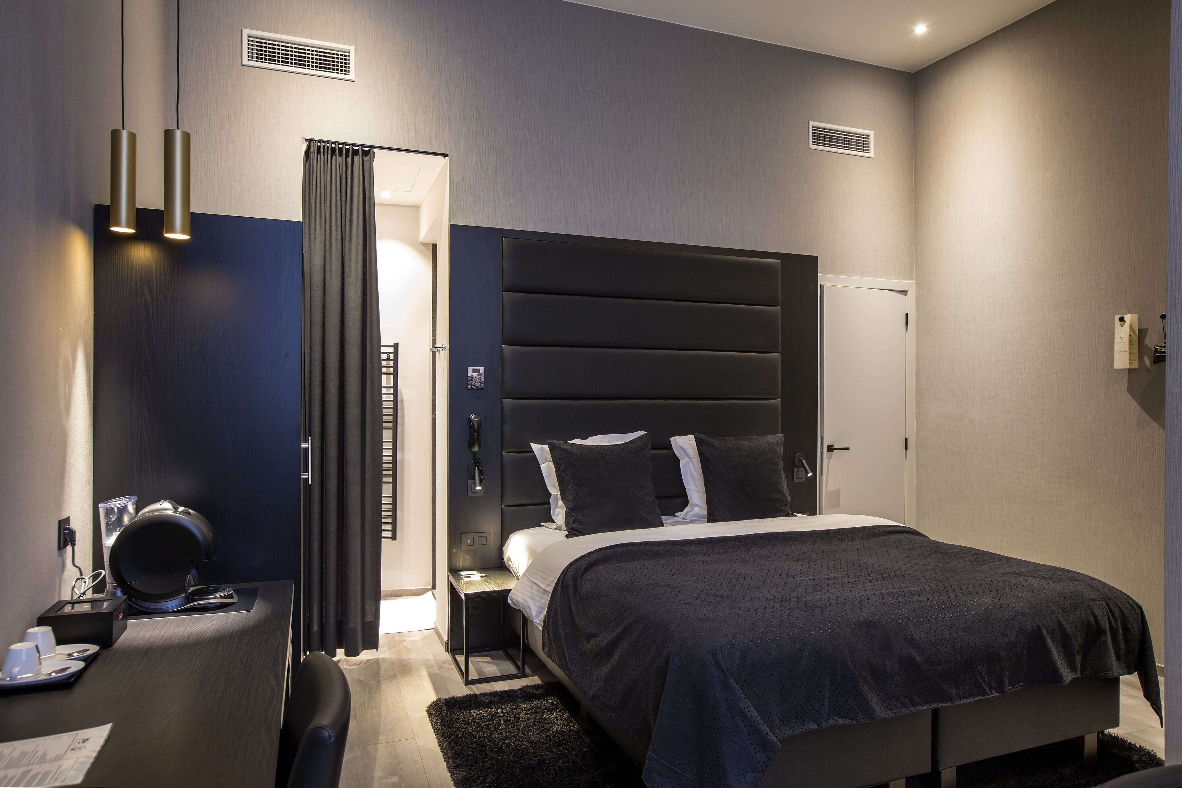 Une chambre d’hôtel moderne avec un grand lit, un bureau avec une chaise et une petite table avec une lampe.