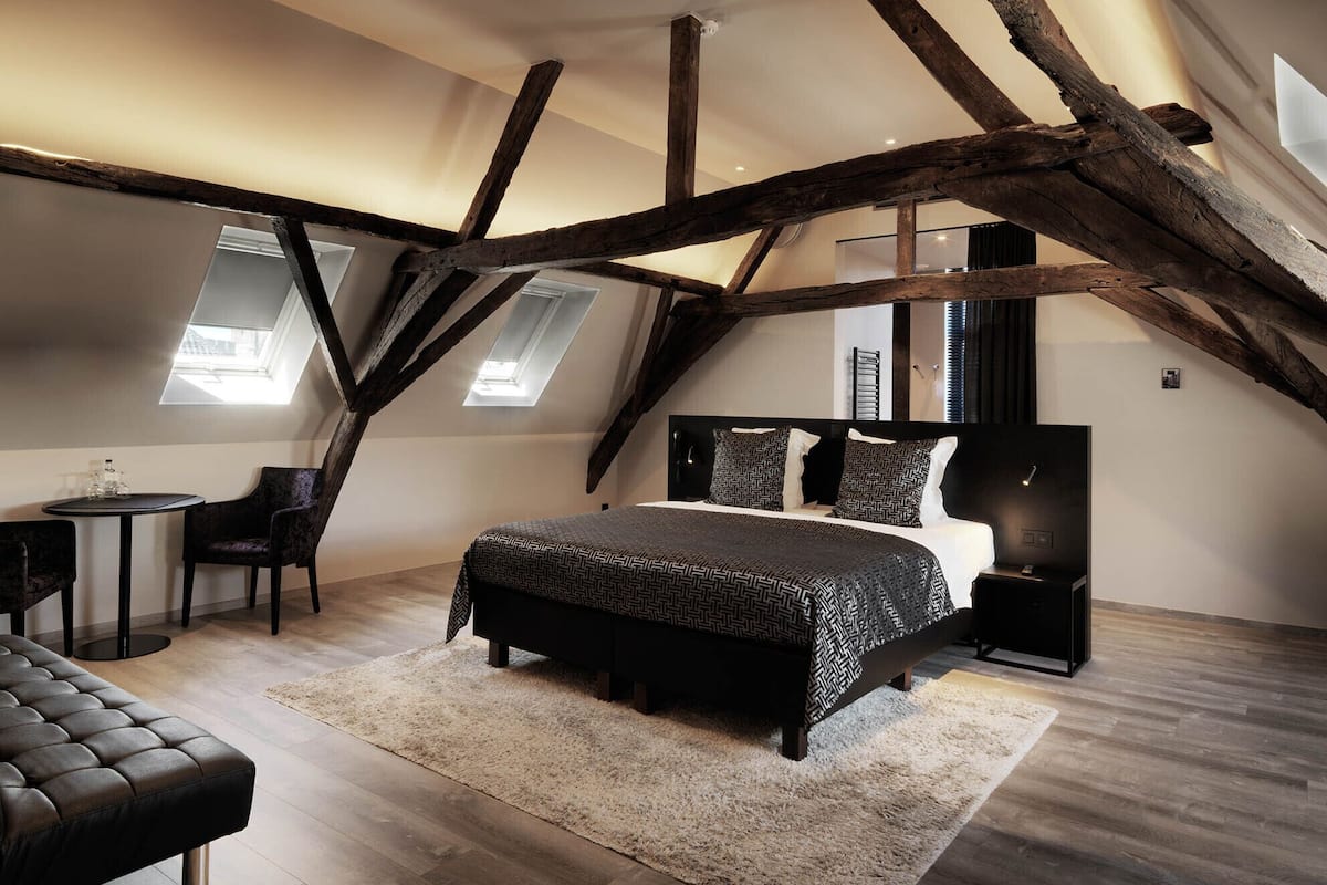 Un dormitorio con una cama grande, un escritorio y una silla. Hay tragaluces y vigas de madera a la vista.