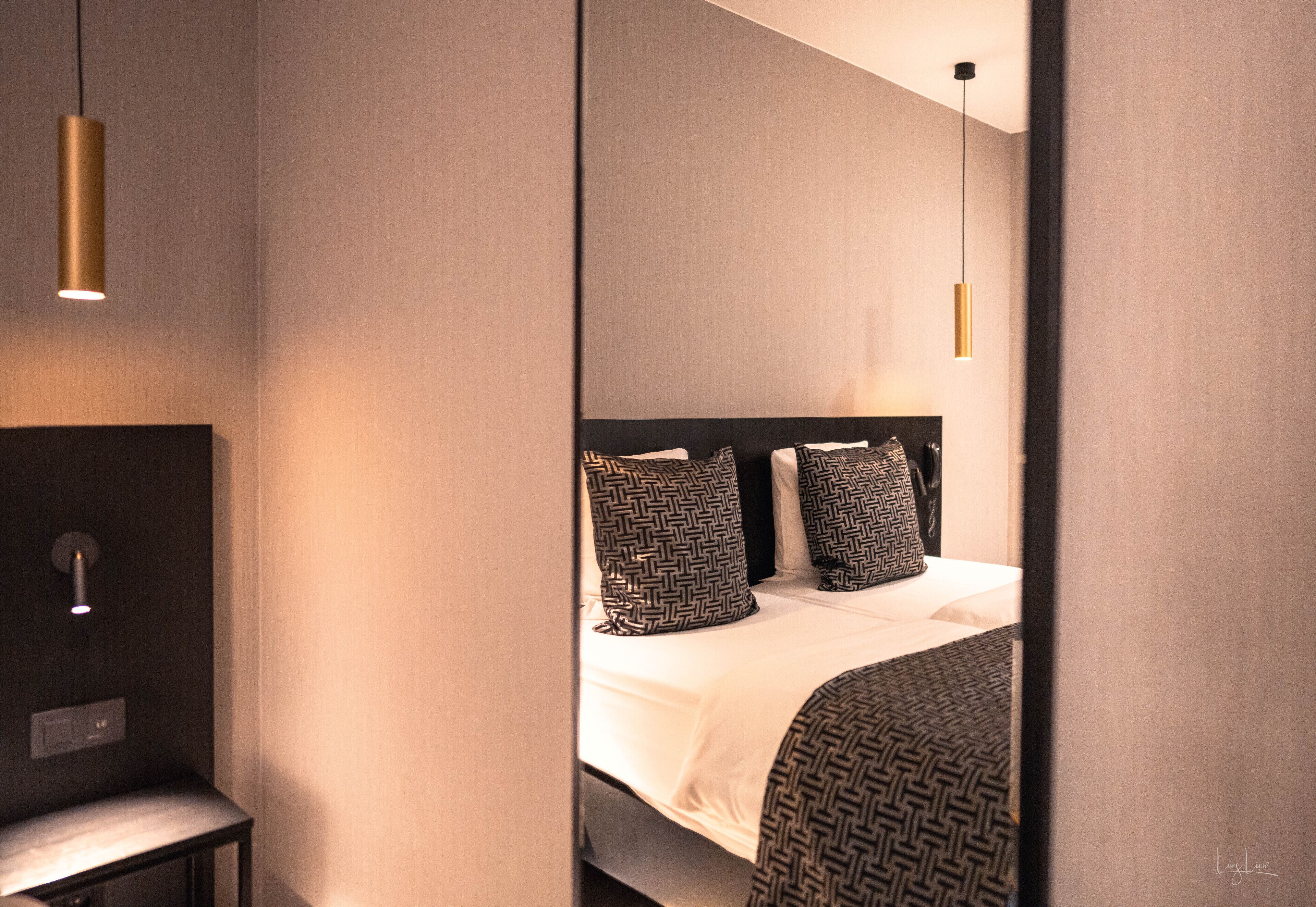 Una habitación de hotel moderna con cama, mesita de noche e iluminación colgante.
