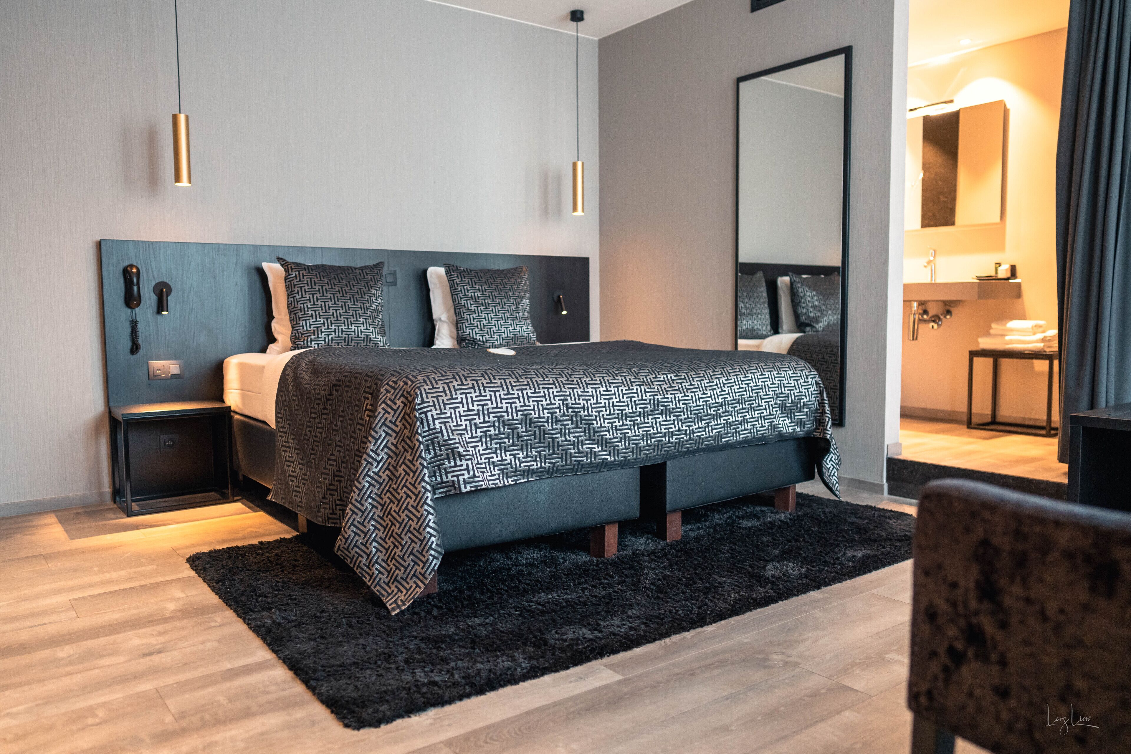 A modern bedroom with a large bed, a bedside table, a nightstand, a black rug, and a mirror above the bed.