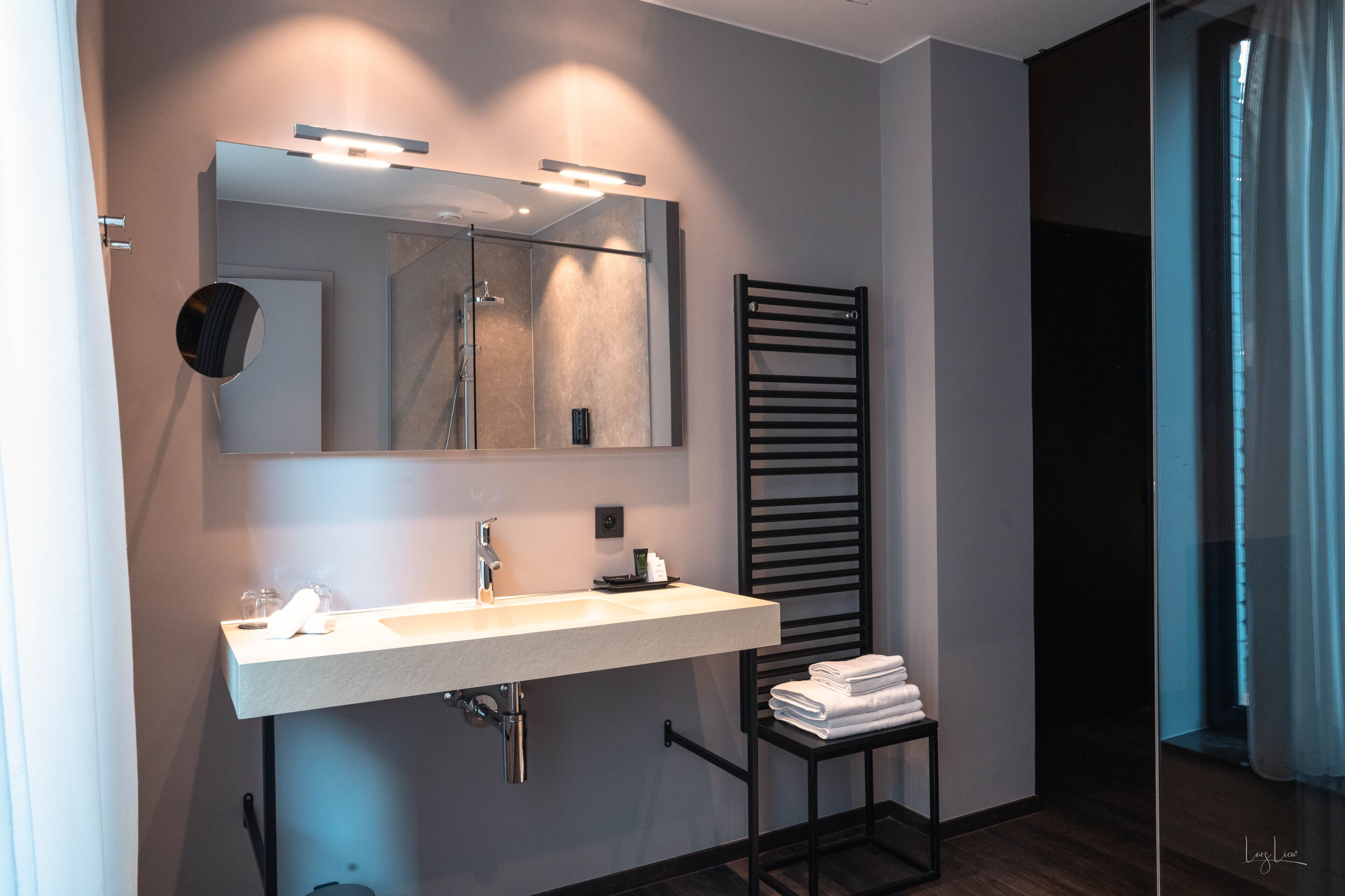A modern bathroom with a large mirror, a sink, and a towel rack.