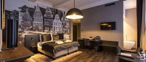 A modern hotel room with a large bed, a desk, a flat-screen TV, and a mural of European architecture.