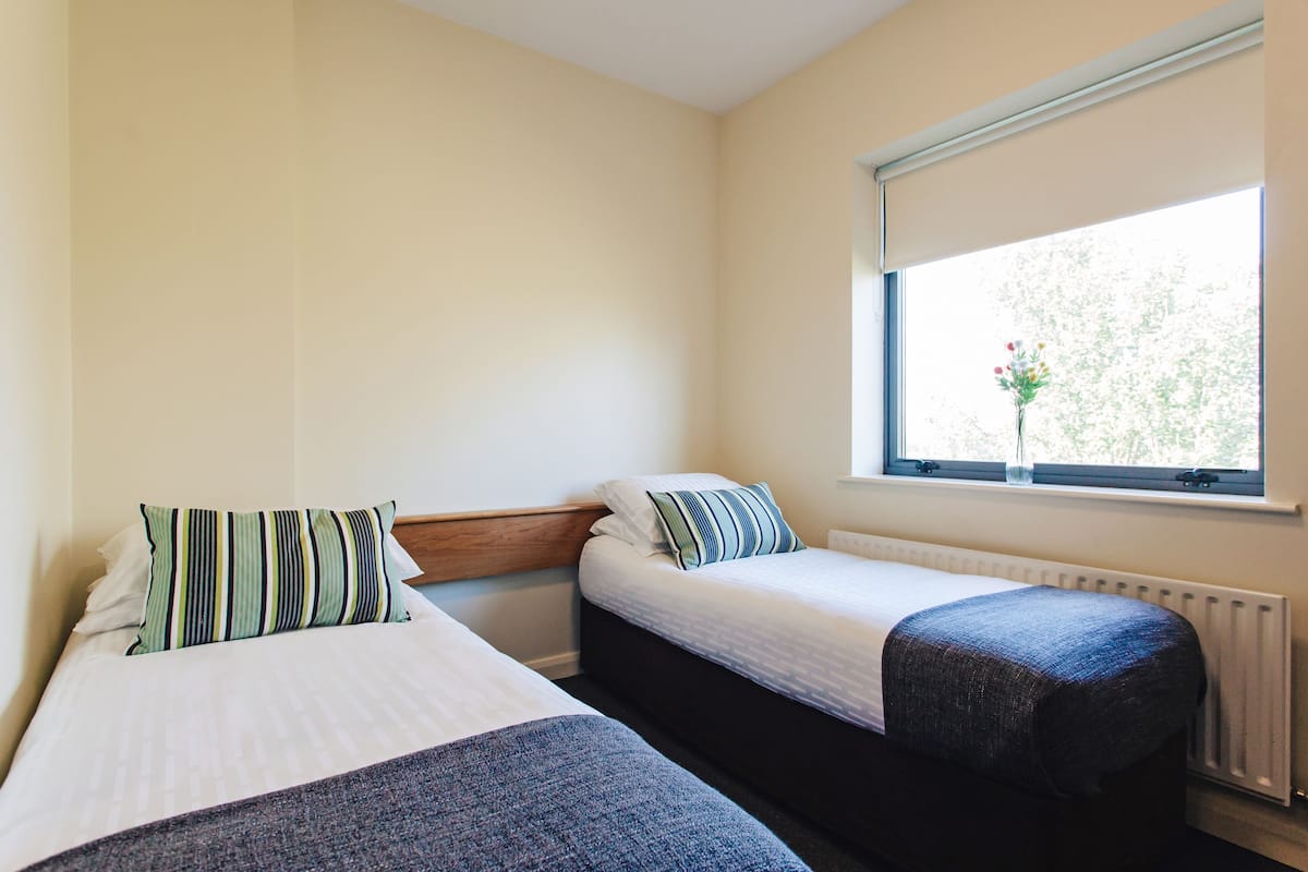A room with two single beds, a window with a view of trees, and a radiator.