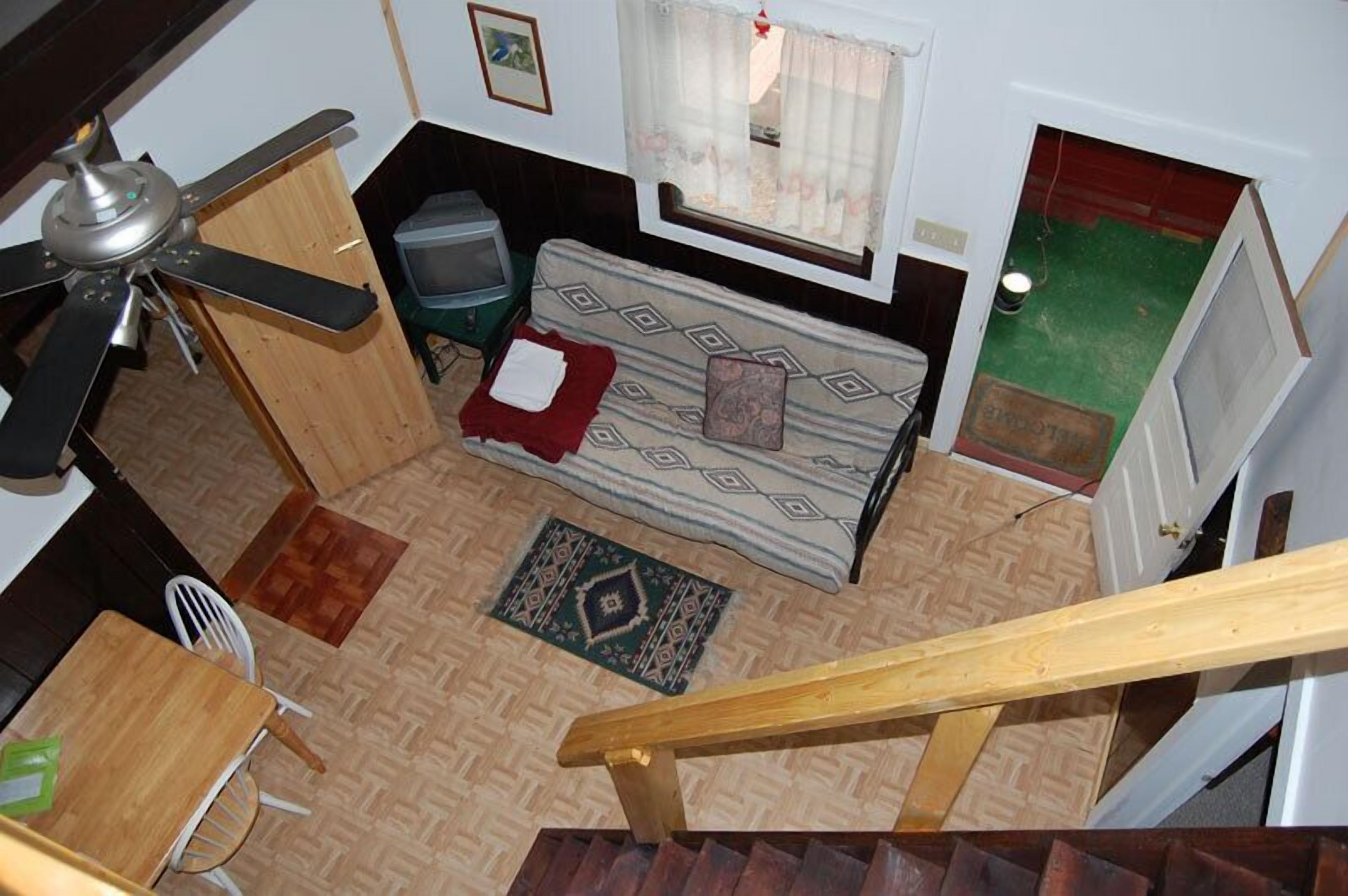 A compact room with a bed, a small table, a chair, a ceiling fan, and a window with curtains.