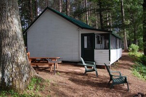 A small cabin with a green roof, a wooden bench, and a chair outside.