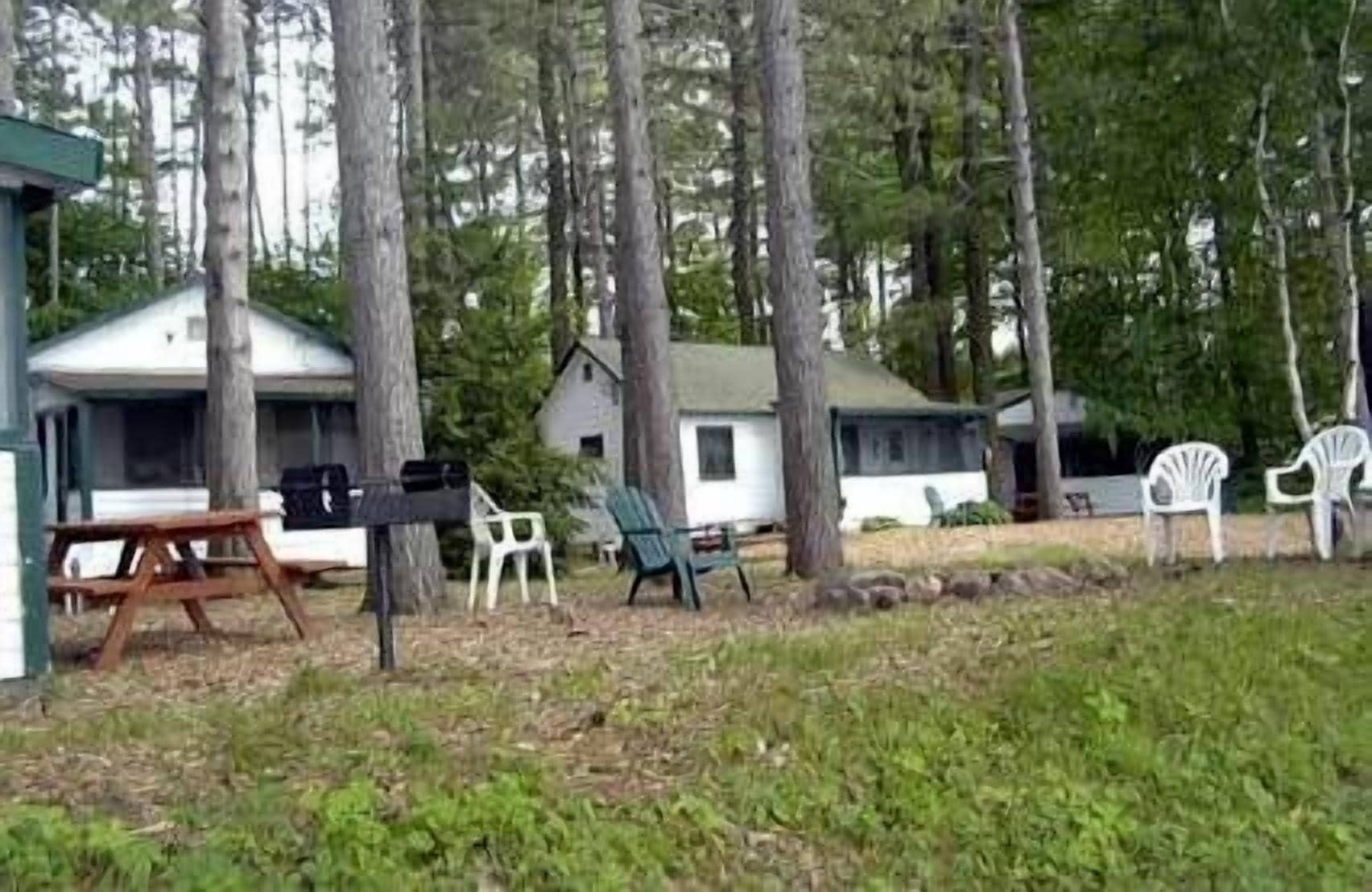 A campsite with cabins, outdoor seating, and trees.