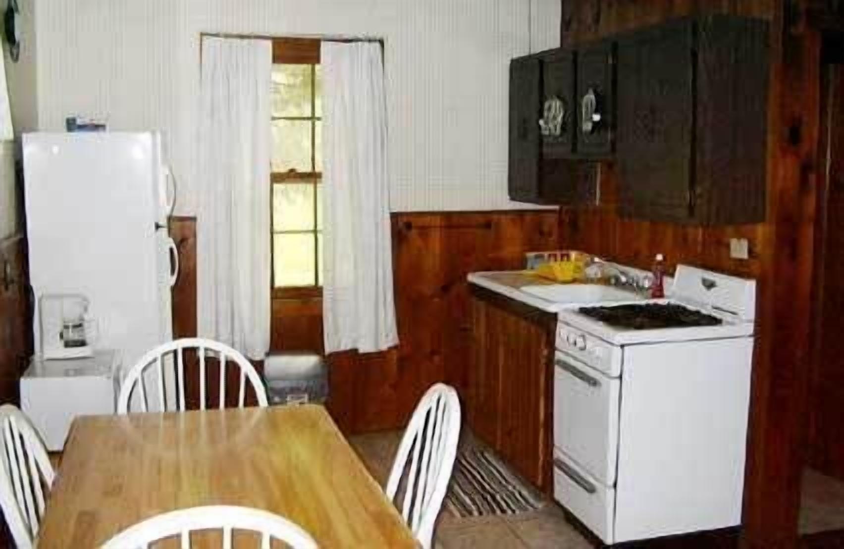 A compact kitchen with a wooden table and chairs, a white refrigerator, a stove, and wooden cabinets.