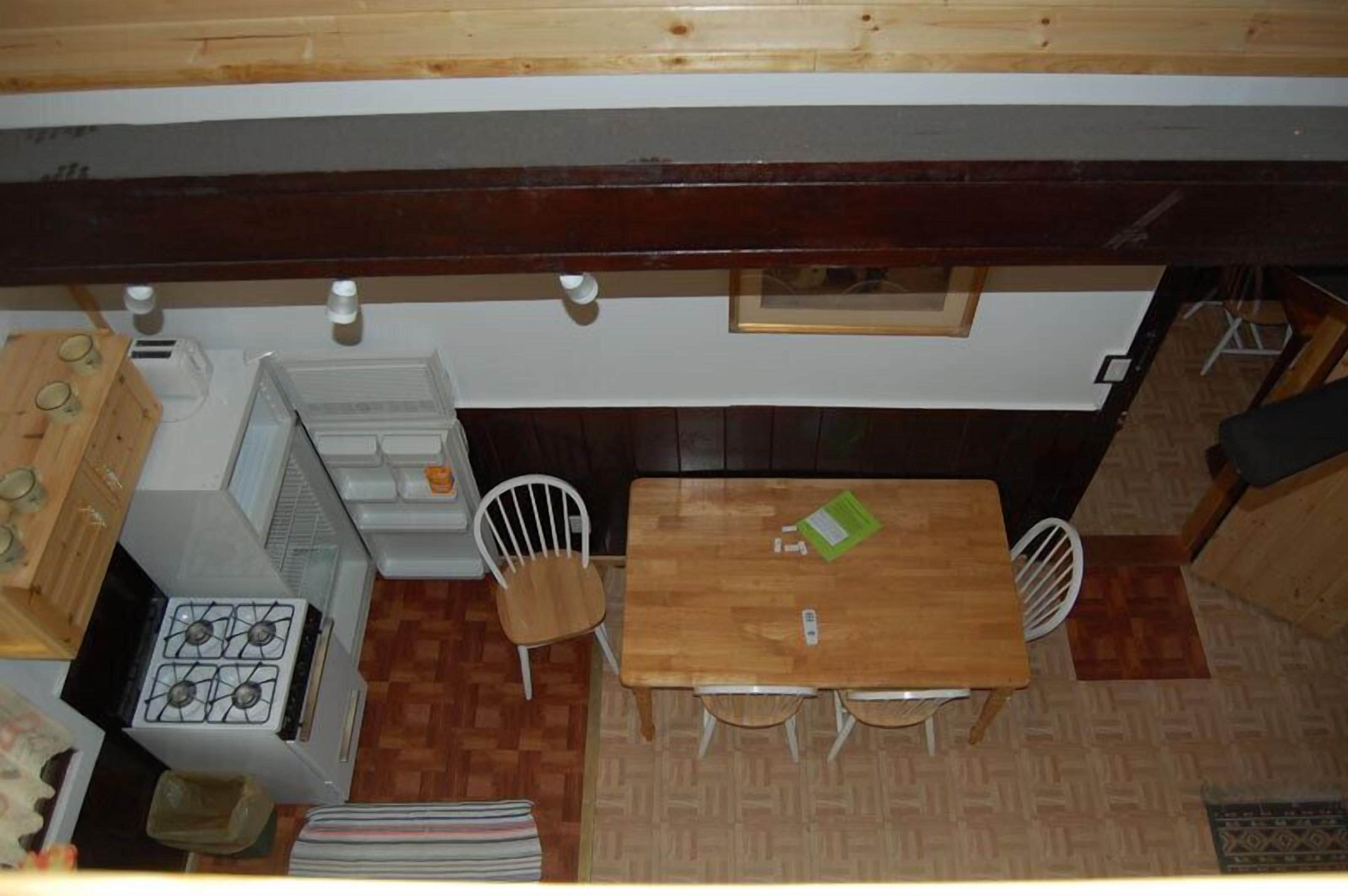 Una cocina compacta con estufa, lavamanos y armarios de madera. Hay una zona de comedor con una mesa y sillas.