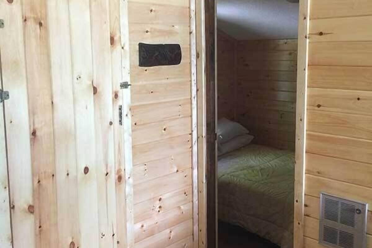 A wooden room with a door, a bed, and a vent.