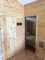 A wooden room with a door, a bed, and a vent.
