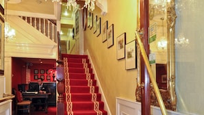 Una imponente escalera con alfombra roja y detalles dorados, que conduce a una habitación con un escritorio y una silla.