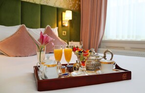 A breakfast tray with a teapot, glasses of orange juice, a fruit bowl, and a sugar bowl on a bed in a hotel room. - Kilronan Guesthouse (Dublin)