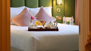 Una cama bien hecha con dos almohadas, una bandeja con alimentos para el desayuno y una mesita de noche con una lámpara.
