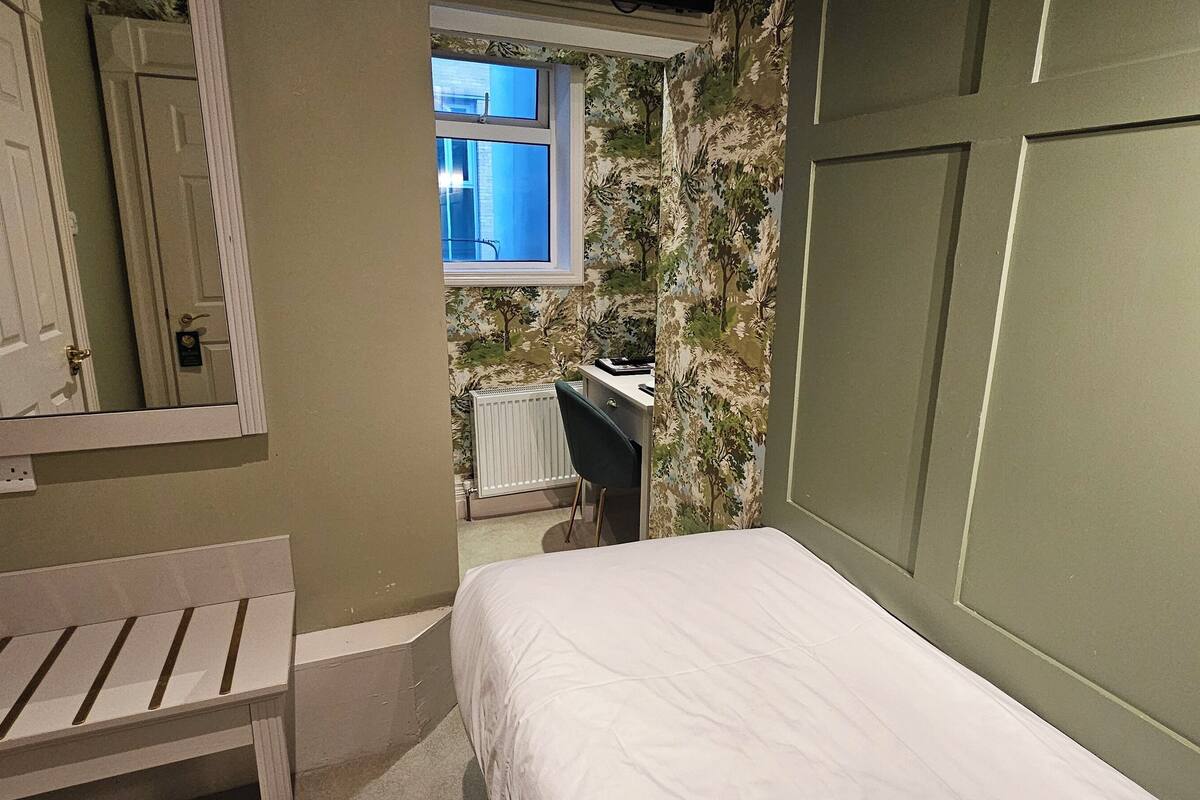 A bedroom with a bed, a bench, a radiator, a window, and a door.