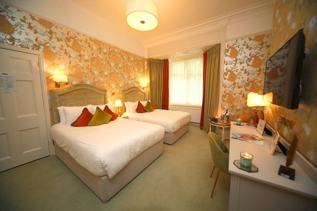 A hotel room with two beds, a desk, a chair, a TV, and a window with curtains.