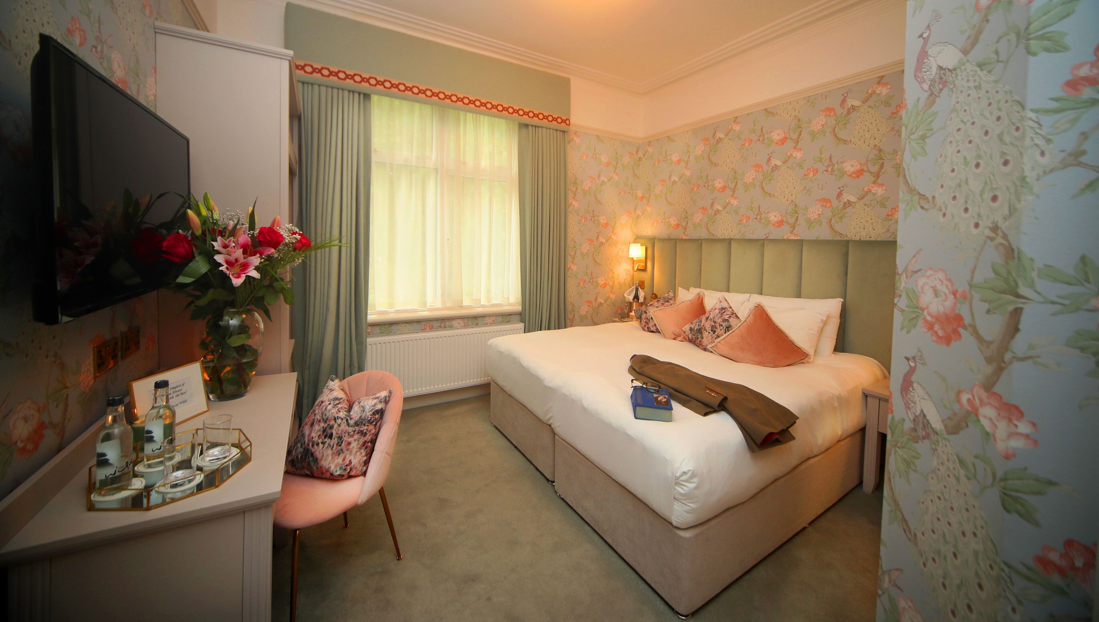 A hotel room with a bed, a desk, a chair, a TV, and a window with curtains.