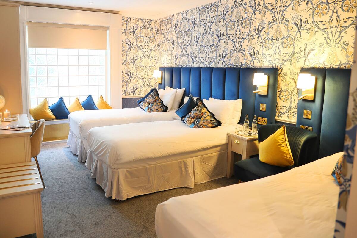 A hotel room with two beds, a desk, and a window.