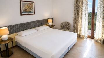 Habitación de hotel con una cama grande, dos mesitas de noche con lámparas, una silla, un cuadro en la pared y vistas a través de las cortinas.