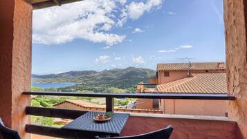 A balcony with a table and chairs, overlooking a scenic landscape with mountains and a body of water.