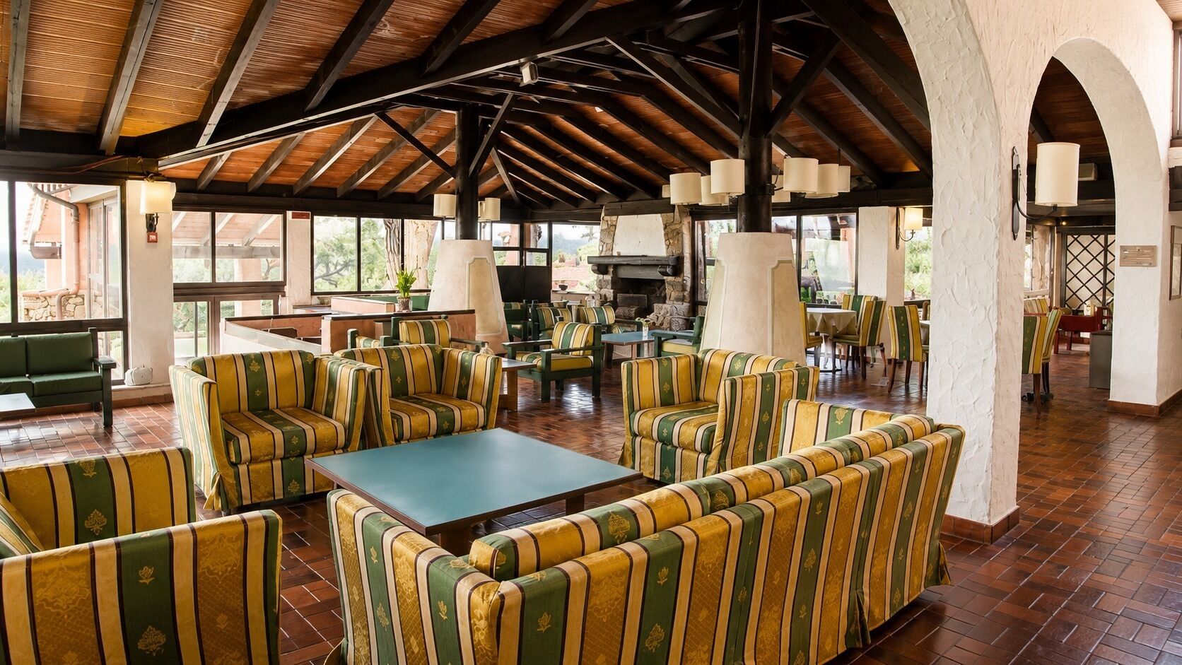 A spacious outdoor seating area with striped sofas and tables, under a wooden roof structure.