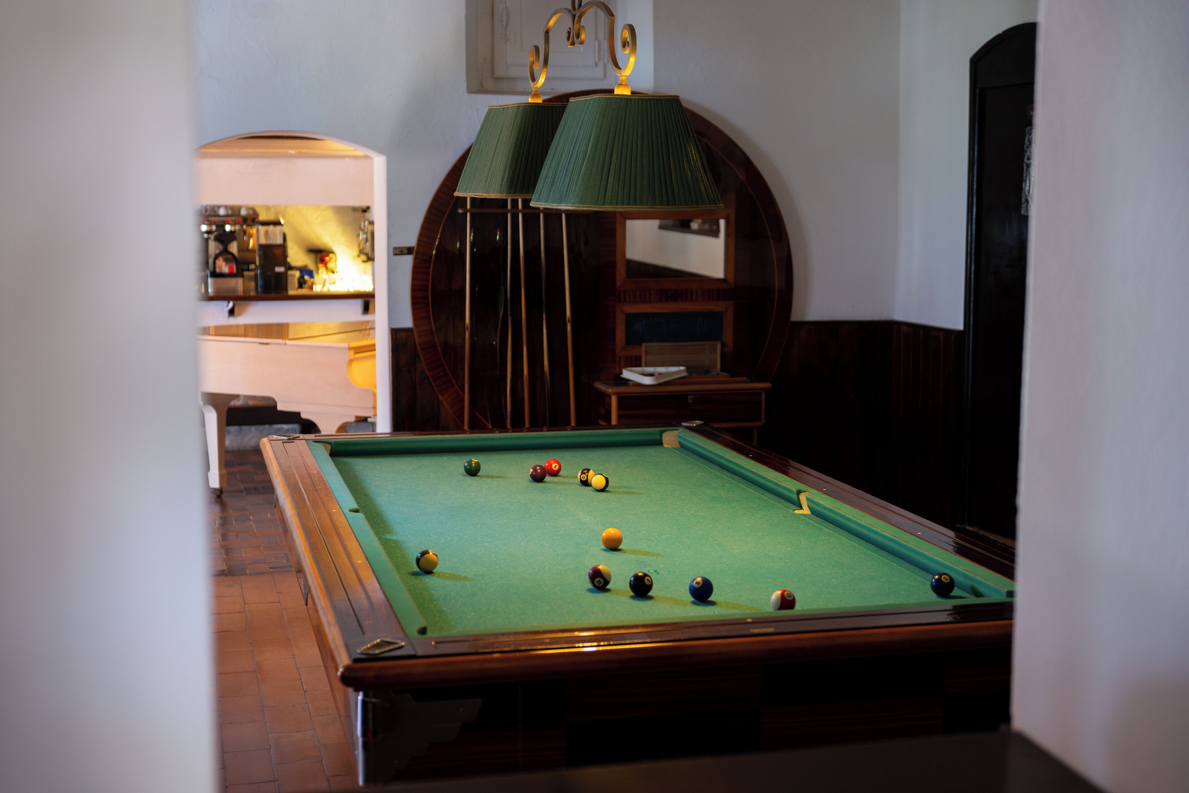 Ein Billardtisch mit Kugeln, ein Spiegel und eine Lampe in einem Raum mit Holzboden.