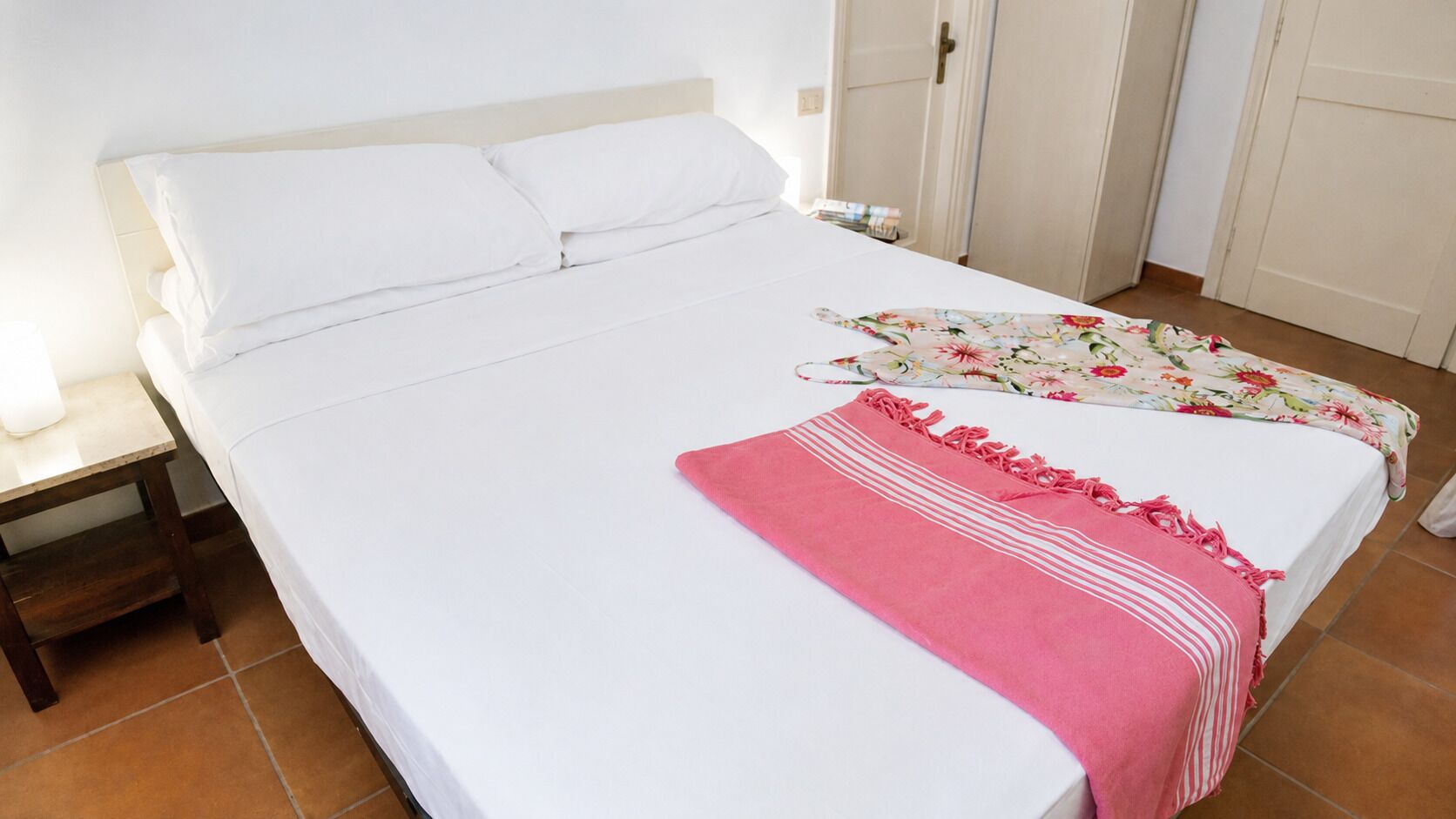 Un letto con biancheria bianca, una coperta rosa e un copripiumino floreale.