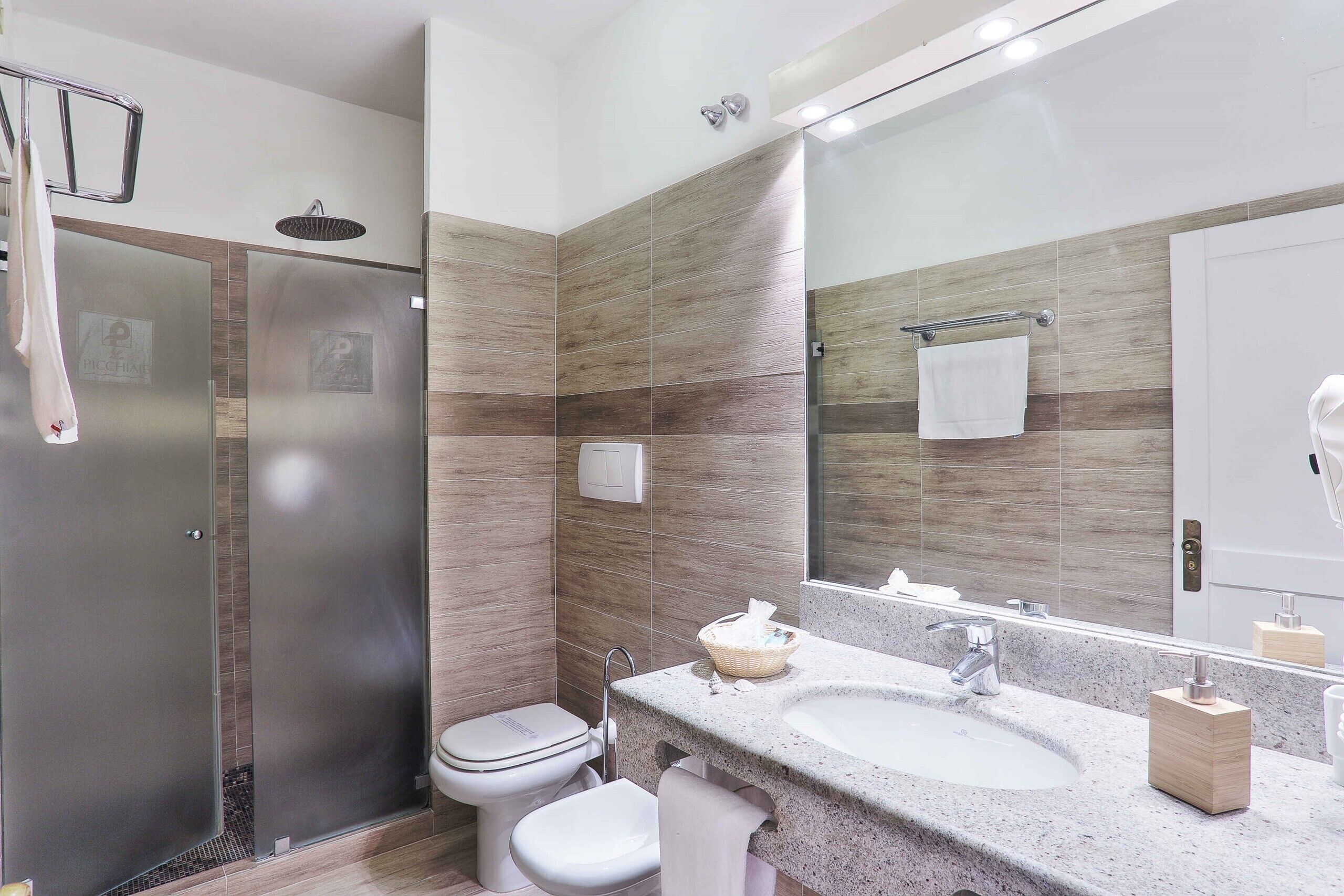 Un baño moderno con ducha, inodoro, lavabo y un espejo grande.