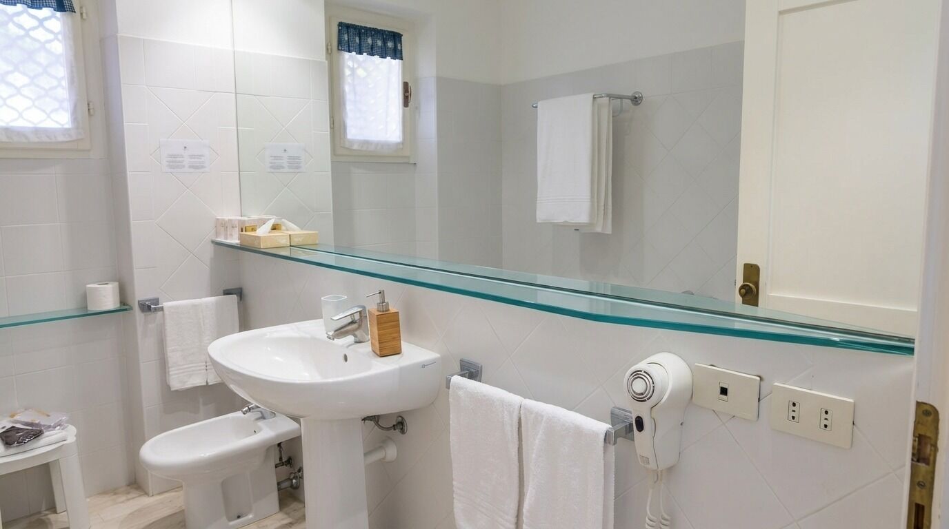 Un baño con lavamanos de vidrio, un bidé, un perchero para toallas, un secador de pelo y un espejo.