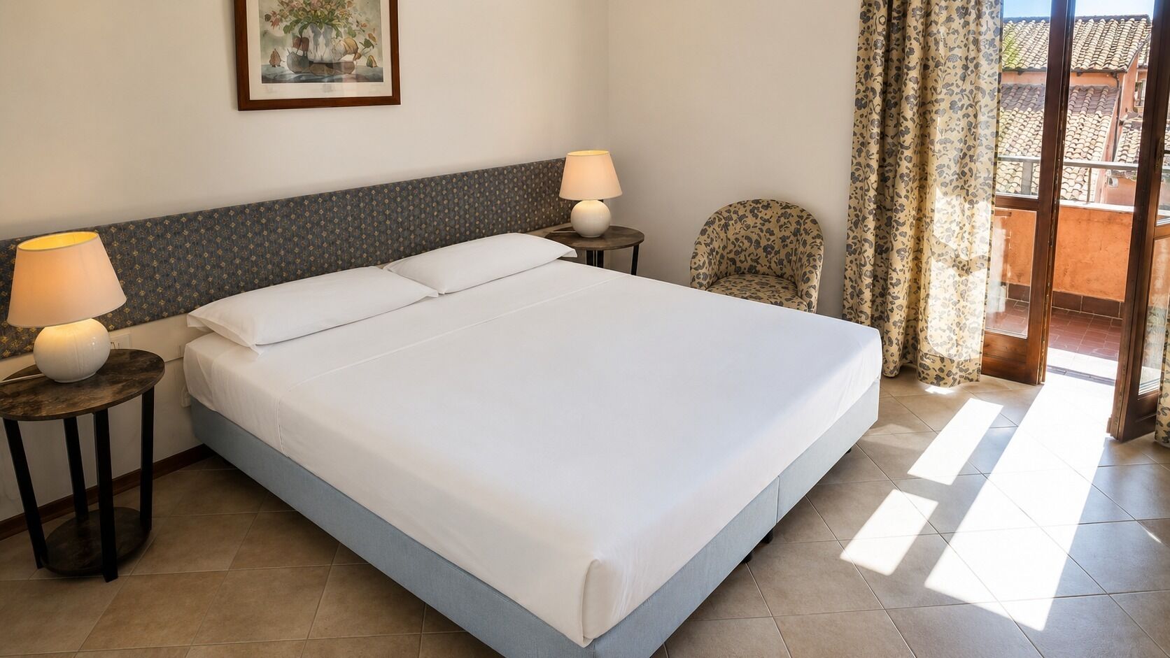 Una camera d'albergo con un letto grande, due comodini con lampade, una sedia e vista all'esterno.