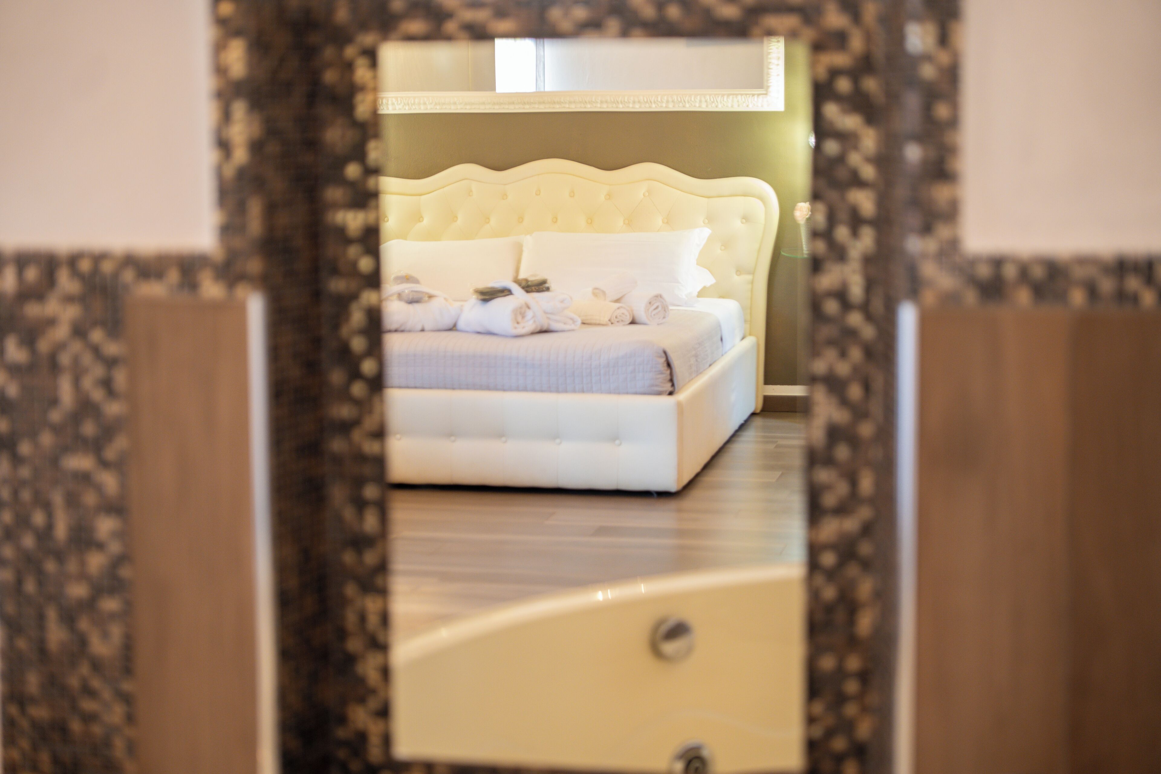 A bed with a tufted headboard, a bedside table, and a mirror above it.