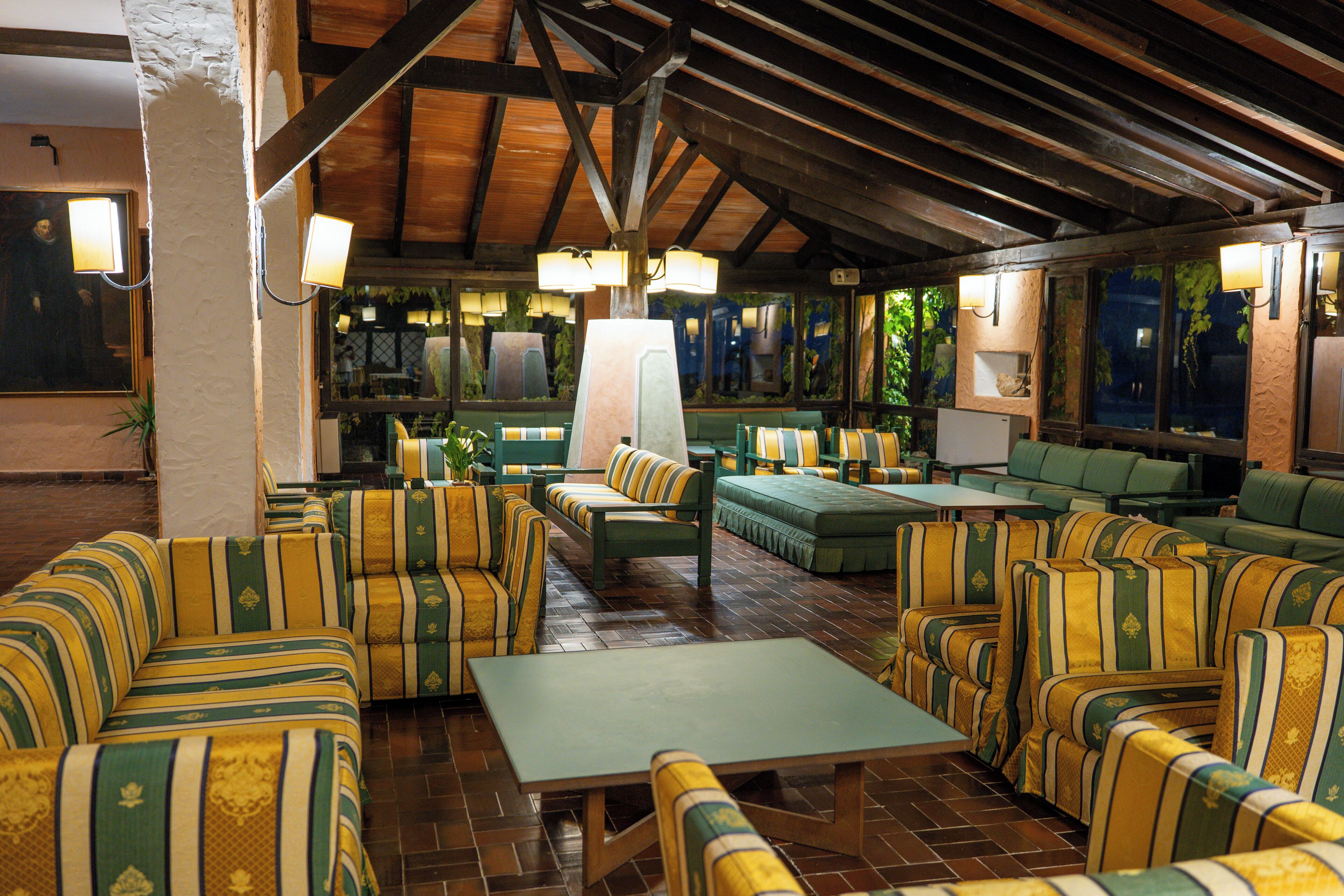 A spacious indoor seating area with multiple couches and tables, wooden beams on the ceiling, and ambient lighting.