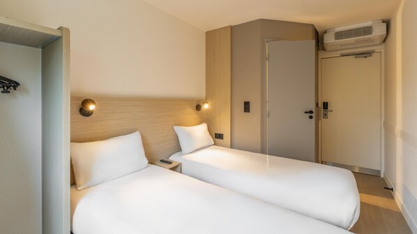 A hotel room with two beds, a wooden headboard, a wall-mounted air conditioner, and a door with a handle.
