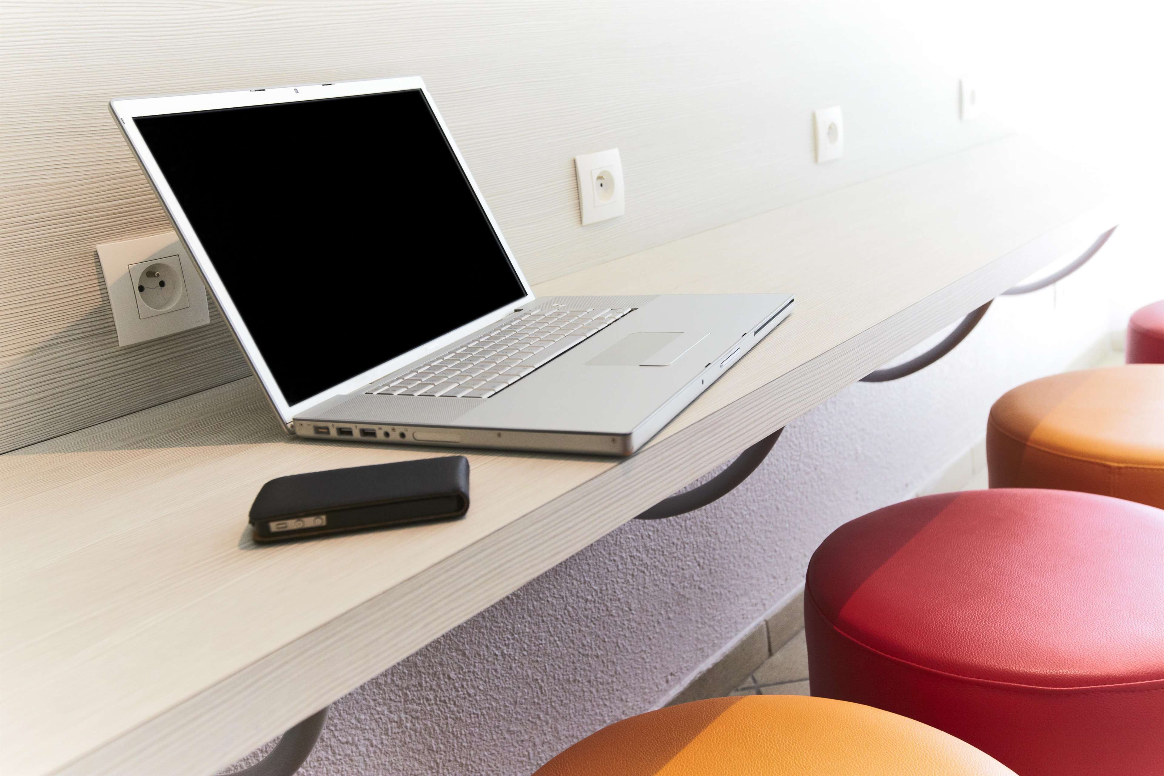 A laptop on a wooden desk with a power outlet, a USB hub, and a red and orange stool.