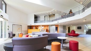 En rymlig entréhall med ett entresolplan, moderna sittgrupper och en centralt placerad dekorativ vägg.
