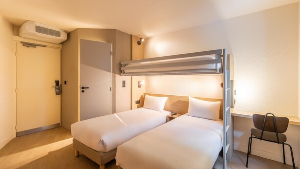 Ett hotellrum med en våningssäng, ett skrivbord, en stol och en väggmonterad luftkonditioneringsanläggning.
