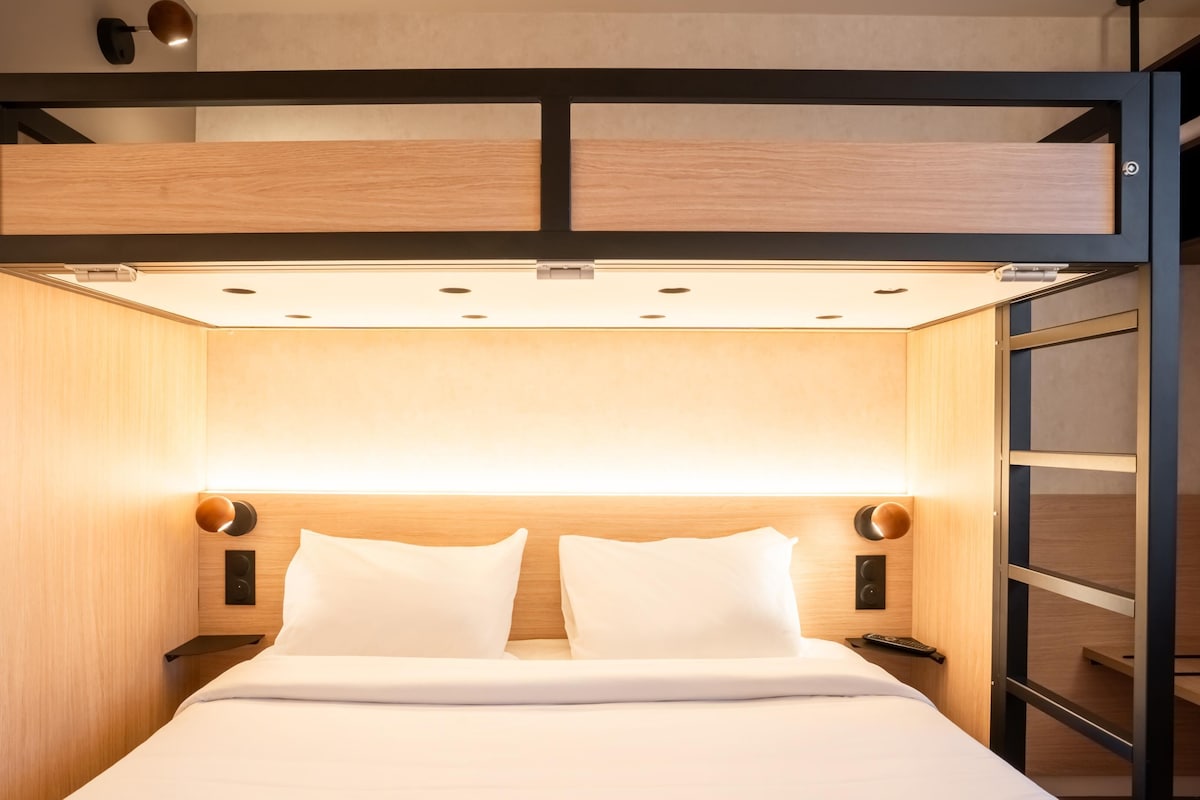 A bunk bed with a wooden headboard, a bedside table, and a wall-mounted light fixture.