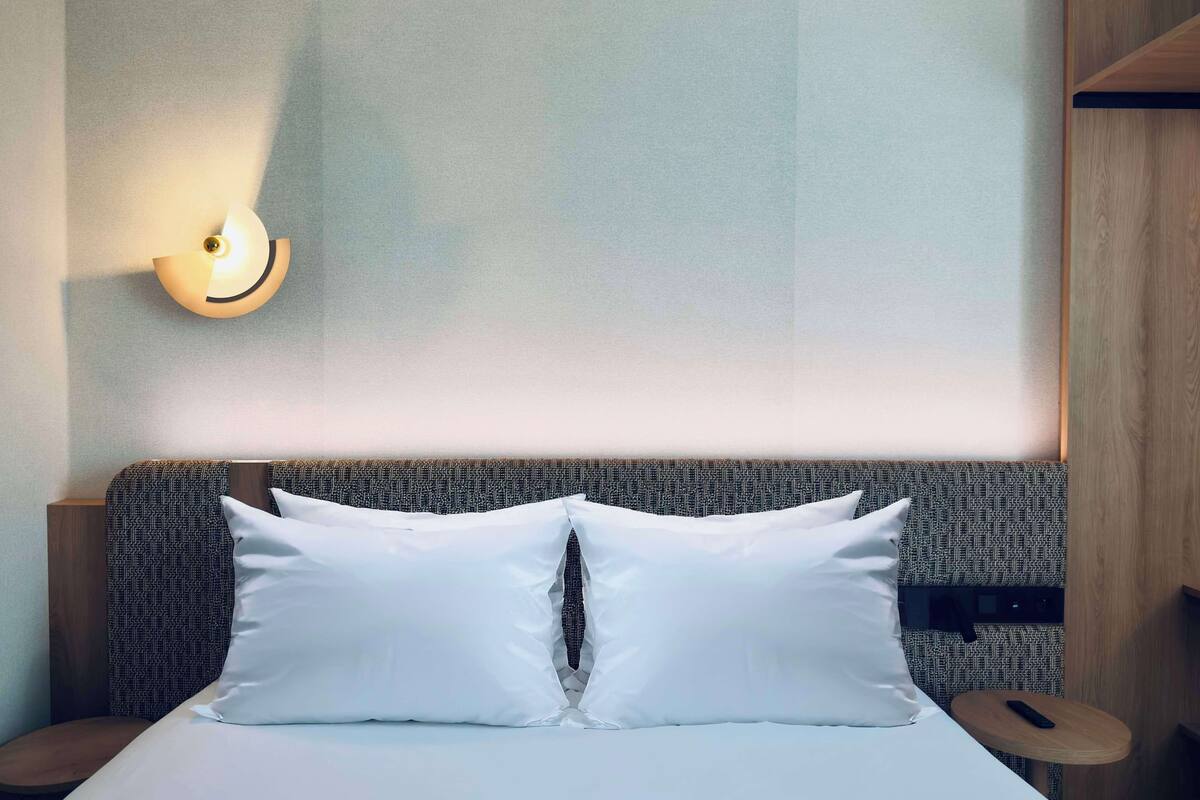 Une chambre d’hôtel avec un lit, une lampe fixée au mur et une petite table.