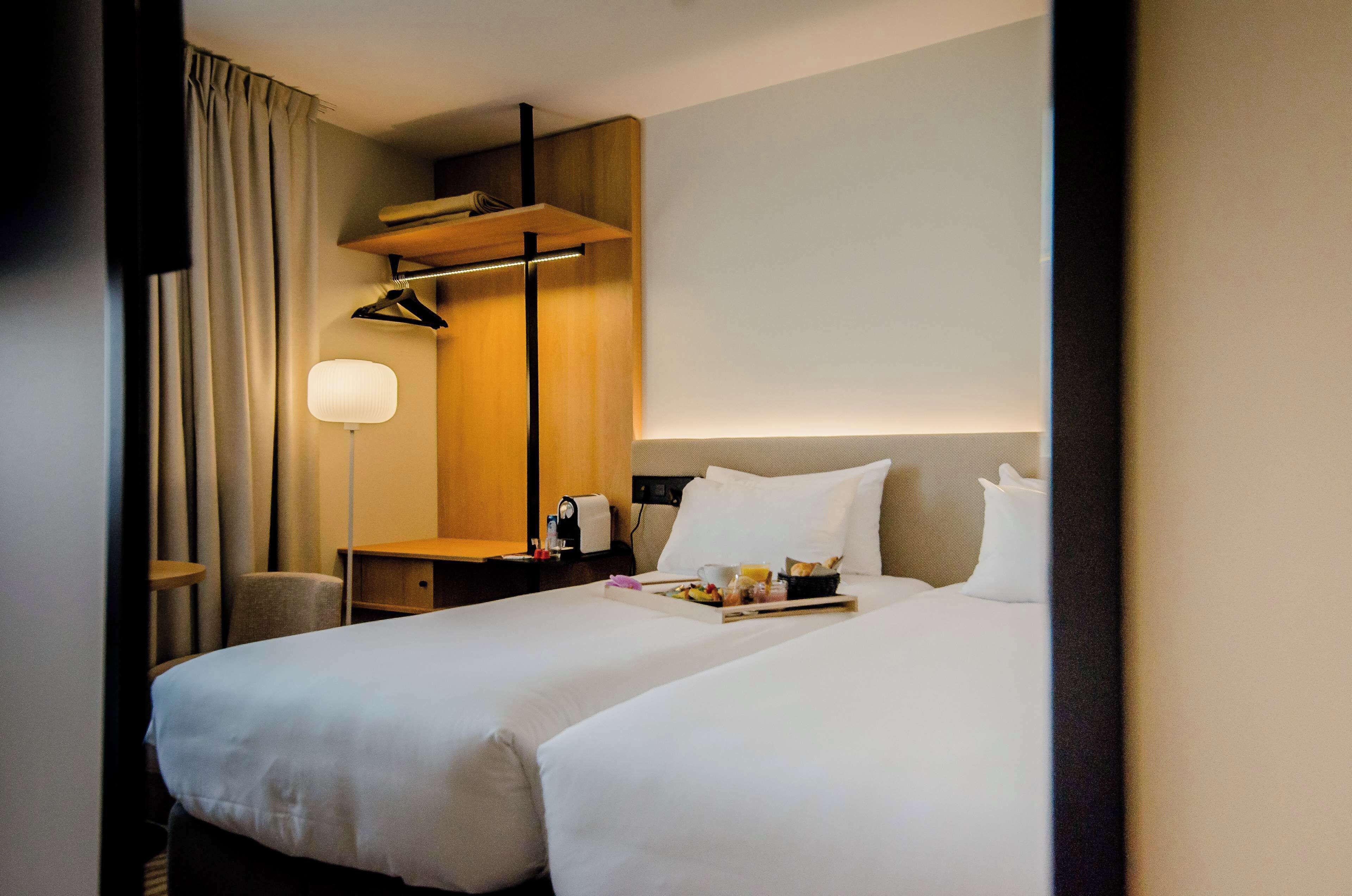 A hotel room with two beds, a desk, a lamp, and a tray with breakfast items.